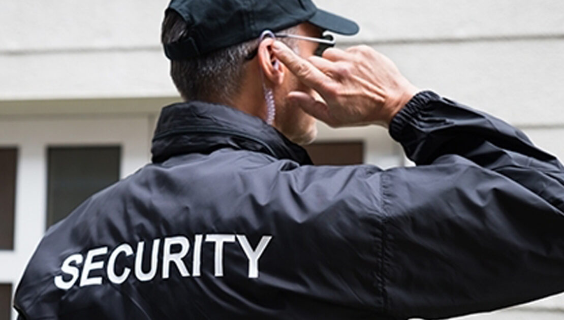 A security guard wearing ear buds and talking on his cell phone.