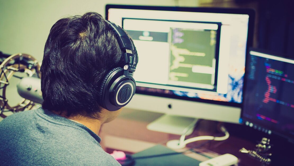 A person with headphones on looking at a computer screen.